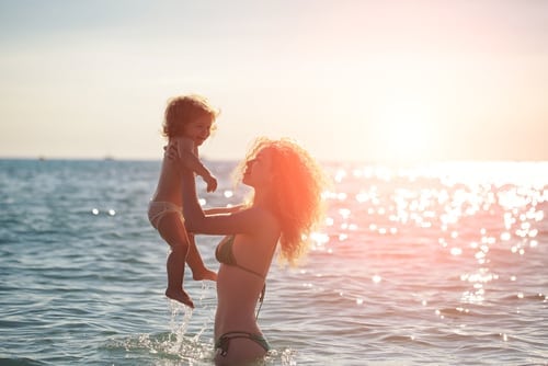 Young mother in bikini standing swimming and playing with male child boy in sea